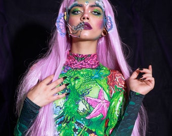 May include: A woman with pink hair and green and pink makeup is wearing a green and pink bodysuit with a sea creature design.