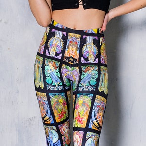 Puede incluir: Leggings negros con un estampado de vitral colorido que presenta varias figuras y diseños. Los leggings los lleva una persona con el pelo negro y una camiseta negra.