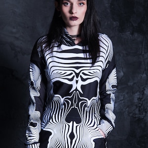 Puede incluir: Sudadera con capucha negra y blanca con un gr&aacute;fico de calavera. La calavera est&aacute; hecha de l&iacute;neas onduladas y gotea por la parte delantera de la sudadera.