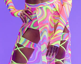 May include: A woman wearing a neon pink and yellow swirl print crop top and matching skirt with a neon green lace-up leg garter. She is wearing white platform boots.
