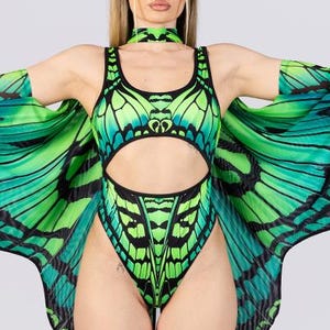 May include: A green and black butterfly-themed bodysuit with matching wings and choker. The bodysuit has a cut-out design and is paired with white platform boots with black laces. The wings are spread wide, showcasing the butterfly pattern.