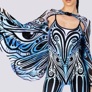 Puede incluir: Un mono con estampado negro y azul con mangas largas a juego y un diseño tipo capa. El mono presenta un diseño simétrico con patrones en forma de ojo y remolinos. El modelo lleva botas de plataforma negras.