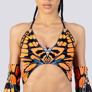 May include: A halter top, shorts, and arm sleeves set with a butterfly wing pattern in orange, black, and blue. The shorts have a ruffled edge and a heart-shaped buckle. The arm sleeves have a flared design.