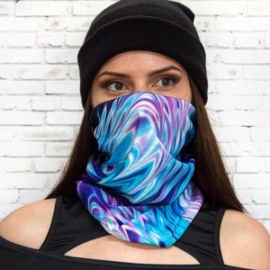 Op de afbeelding: Een zwarte beanie met een blauw, paars en wit gepatroneerd gezichtsmasker. Het masker wordt gedragen door een persoon met lang bruin haar. De persoon draagt een zwart top met blote schouders.