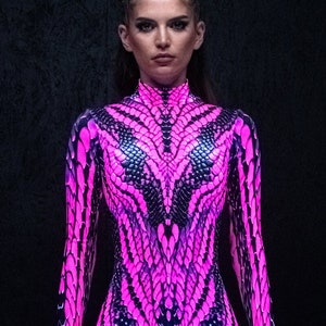 May include: A woman wearing a pink and black snakeskin print bodysuit. The bodysuit has long sleeves and a high neck.