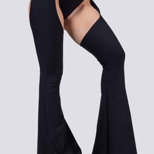 May include: Black flared pants with thigh cutouts. The pants feature a high waist and are paired with platform shoes. The design includes a unique open-leg style, offering a bold and modern look. The fabric appears to be a smooth, stretchy material.