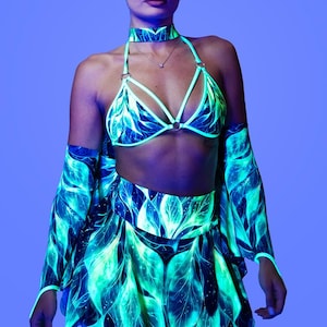 Può includere: Un completo a due pezzi composto da un top bikini a triangolo con girocollo e una gonna abbinata, entrambi decorati con un motivo a foglie verde e blu luminescente su sfondo scuro, completato da maniche abbinate.