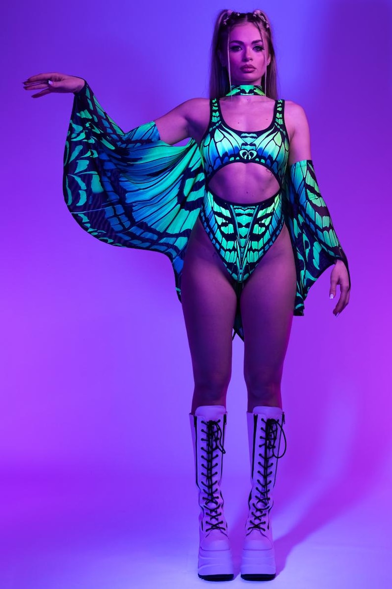 May include: A neon green and blue butterfly-themed bodysuit with matching cape sleeves and a choker. The outfit is paired with white platform boots. The design features a butterfly wing pattern. The background is a gradient of purple and pink.