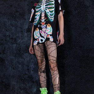May include: A black t-shirt with a colorful skeleton graphic. The skeleton is decorated with flowers and other patterns. The model is wearing black fishnet tights and bright green platform boots.