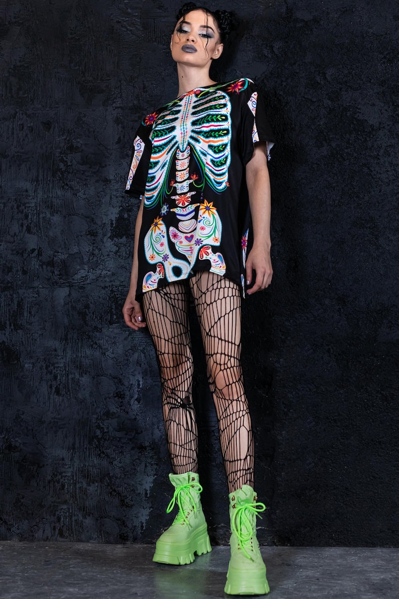 May include: A black t-shirt with a colorful skeleton graphic. The skeleton is decorated with flowers and other patterns. The model is wearing black fishnet tights and bright green platform boots.