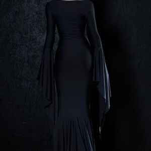 May include: A black maxi dress with long sleeves and a flowing skirt. The dress has a fitted bodice and a scoop neckline.