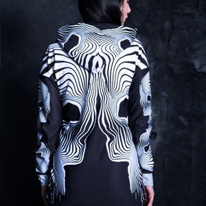 Puede incluir: Vestido negro y blanco con capucha y estampado de calavera. El vestido tiene manga larga y una silueta ajustada.