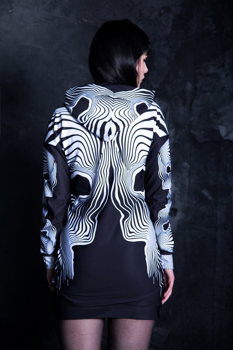 Puede incluir: Vestido negro y blanco con capucha y estampado de calavera. El vestido tiene manga larga y una silueta ajustada.