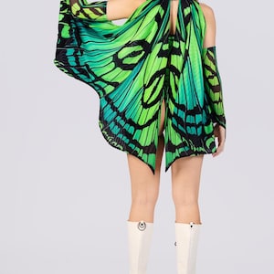 May include: A green and black butterfly wing costume with matching arm sleeves. The costume is worn with white platform boots. The butterfly wings are a vibrant green with black detailing, creating a striking visual effect. The outfit is designed to resemble butterfly wings.