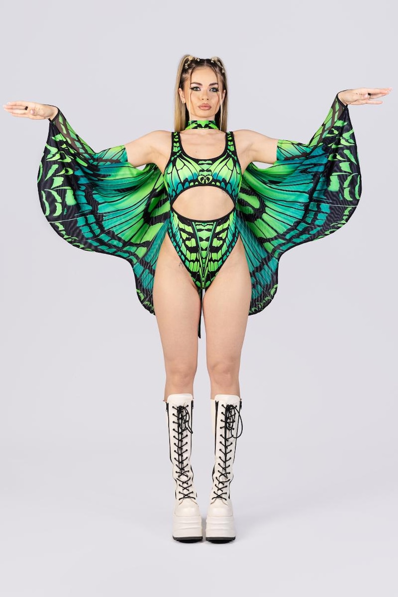 May include: A green and black butterfly-themed bodysuit with matching wings and choker. The bodysuit has a cut-out design and is paired with white platform boots with black laces. The wings are spread wide, showcasing the butterfly pattern.