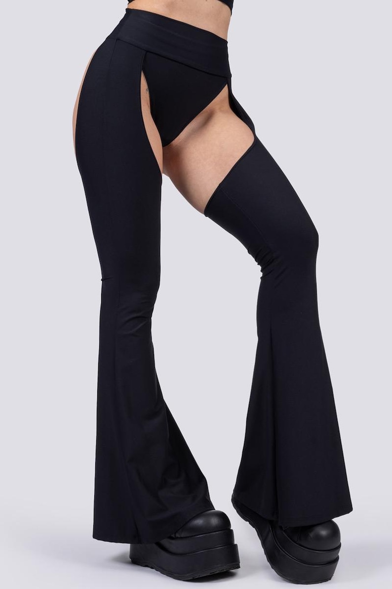 May include: Black flared pants with thigh cutouts. The pants feature a high waist and are paired with platform shoes. The design includes a unique open-leg style, offering a bold and modern look. The fabric appears to be a smooth, stretchy material.