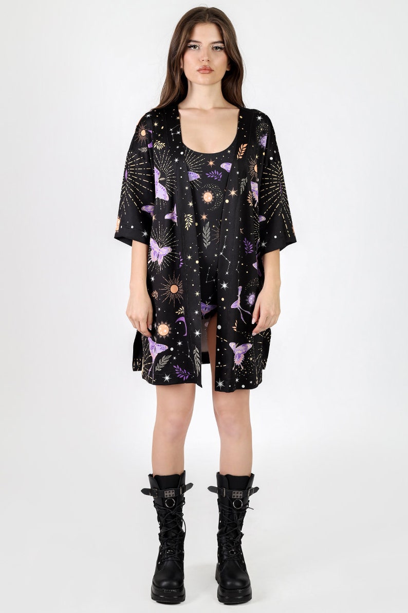 May include: A black kimono with a celestial print featuring butterflies, stars, and moons. The kimono has a short sleeve and is made of a silky fabric.