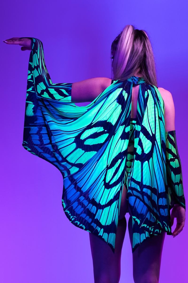 May include: A vibrant, butterfly-wing-inspired garment in shades of teal, blue, and black. The design features intricate patterns resembling butterfly wings, with a halter-style neckline and open back. The sleeves are long and flowing, creating a dramatic effect.
