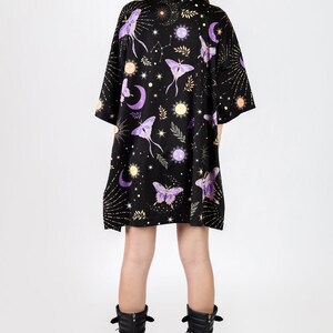 May include: A black t-shirt dress with a celestial print featuring moons, stars, and purple moths. The dress has a relaxed fit and short sleeves.