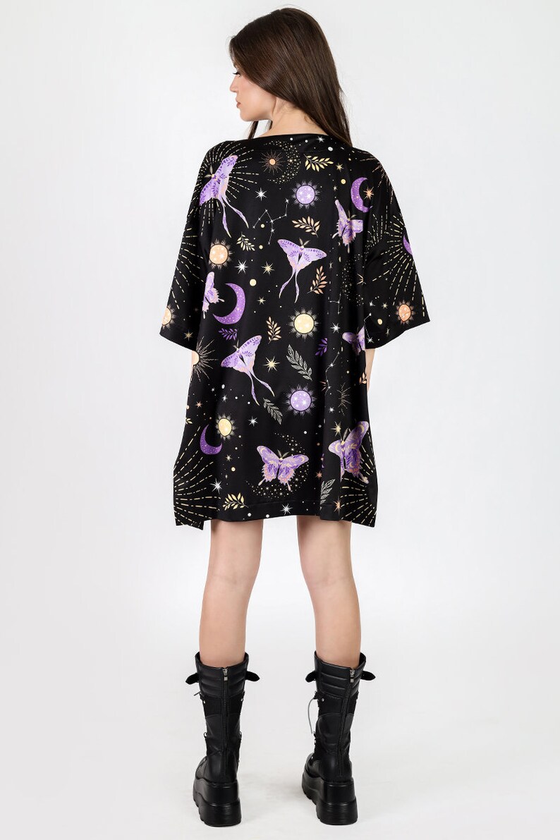 May include: A black t-shirt dress with a celestial print featuring moons, stars, and purple moths. The dress has a relaxed fit and short sleeves.