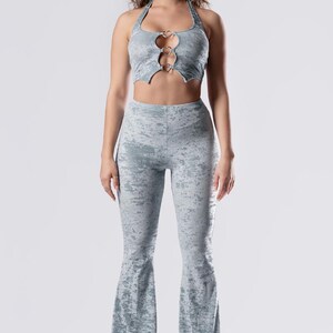 Op de afbeelding: Een lichtblauwe twee-delige outfit met een haltertop met een hartvormige uitsnijding en zilveren ringen. De broek is flared en heeft een subtiele distressed look.