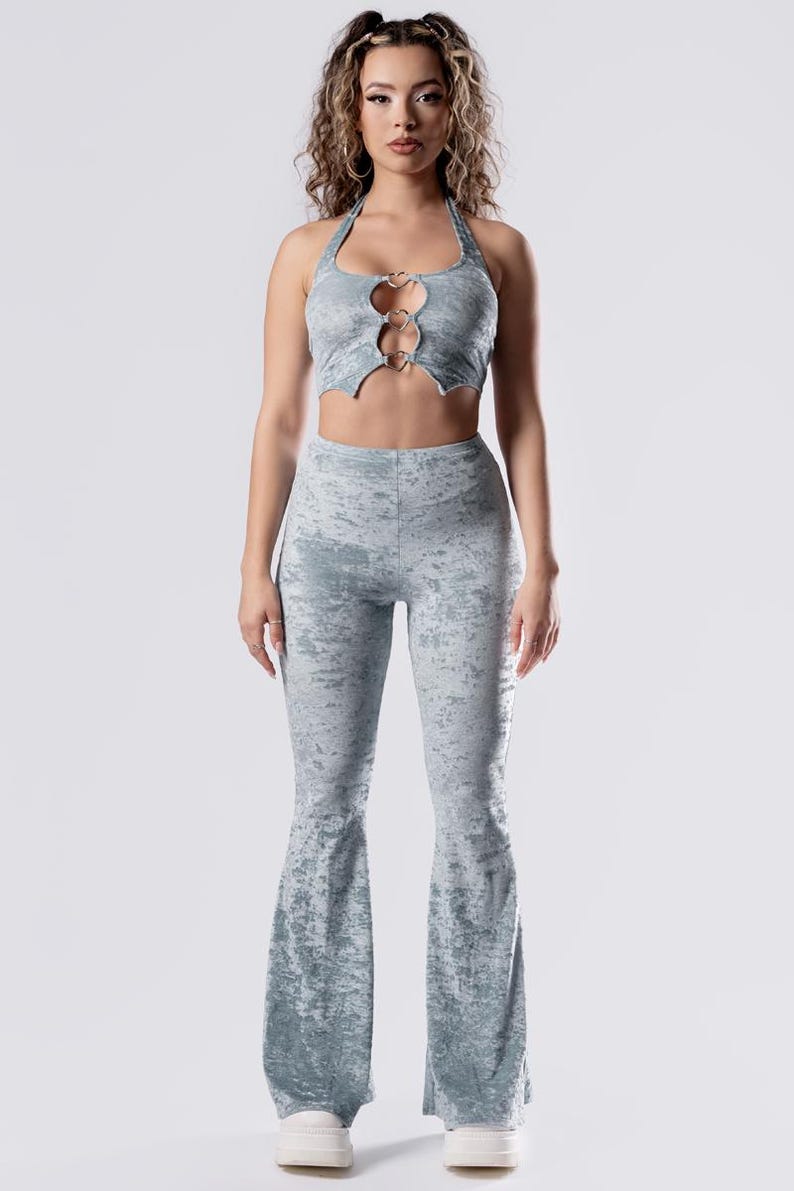 Op de afbeelding: Een lichtblauwe twee-delige outfit met een haltertop met een hartvormige uitsnijding en zilveren ringen. De broek is flared en heeft een subtiele distressed look.