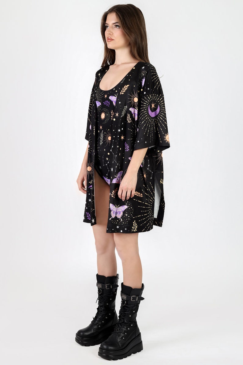 May include: A black kimono with a celestial print featuring butterflies, moons, stars, and suns. The kimono has long sleeves and a side slit. The model is wearing black boots.