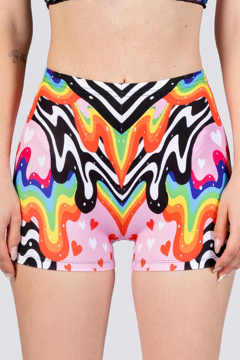 May include: Shorts with a vibrant, colorful design. The shorts feature a pink base with small white and red hearts. A rainbow pattern with black and white wavy lines is the main design element. The shorts are made of a stretchy material.