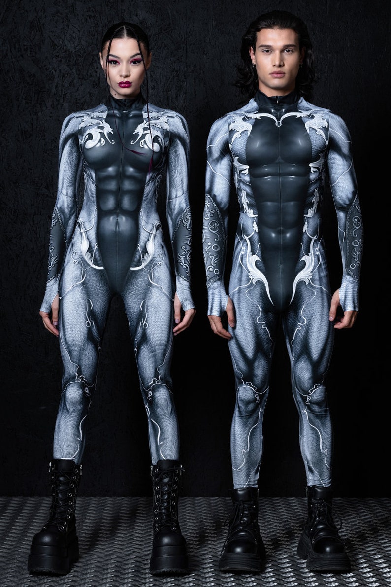 May include: Two people wearing black and white printed full-body suits with a muscular design. The suits have a white pattern of stylized lines and shapes. Both people are wearing black boots.