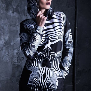 Puede incluir: Sudadera con capucha negra y blanca con un dise&ntilde;o de calavera. La calavera est&aacute; formada por l&iacute;neas onduladas y la sudadera tiene un cord&oacute;n.
