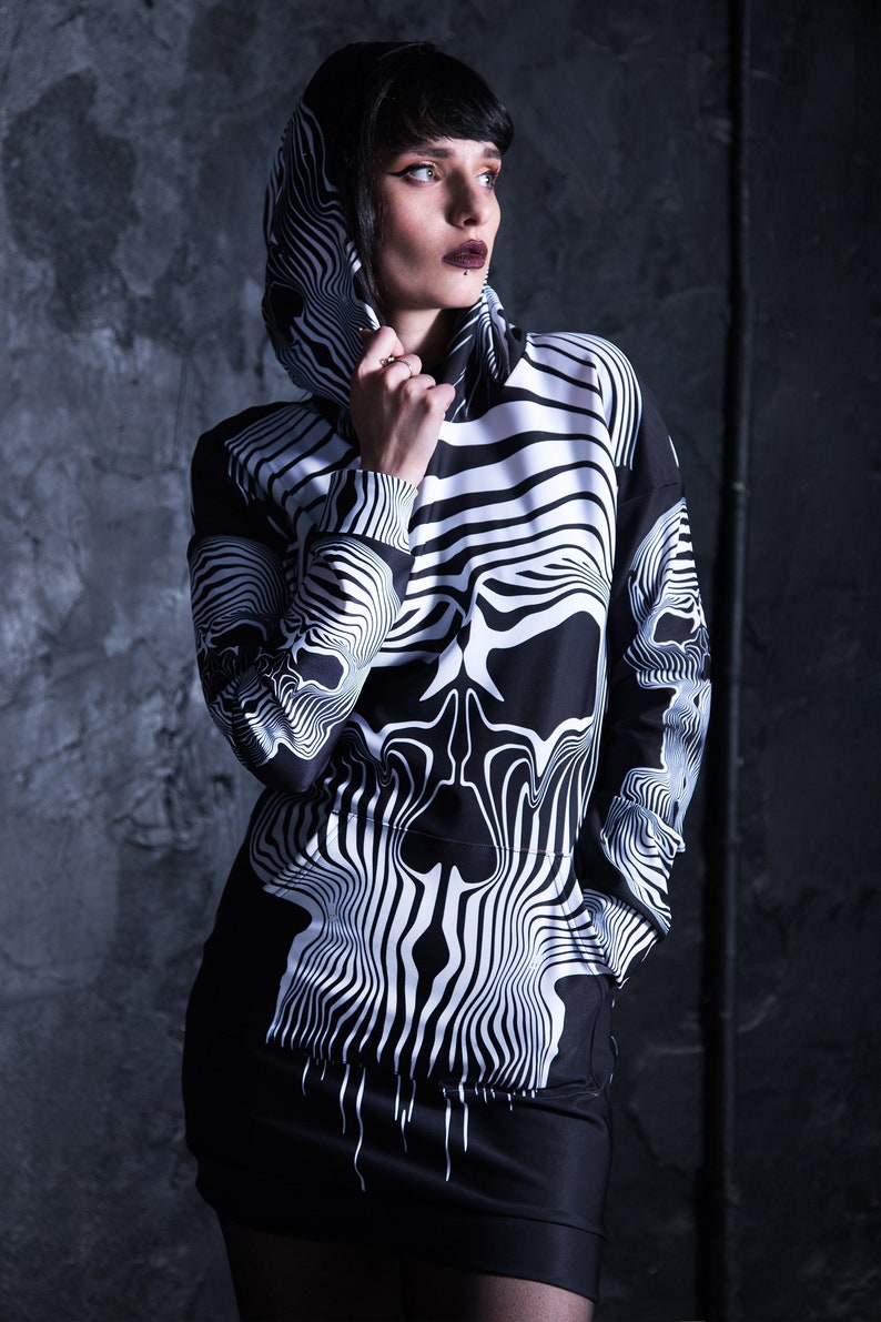 Puede incluir: Sudadera con capucha negra y blanca con un dise&ntilde;o de calavera. La calavera est&aacute; formada por l&iacute;neas onduladas y la sudadera tiene un cord&oacute;n.