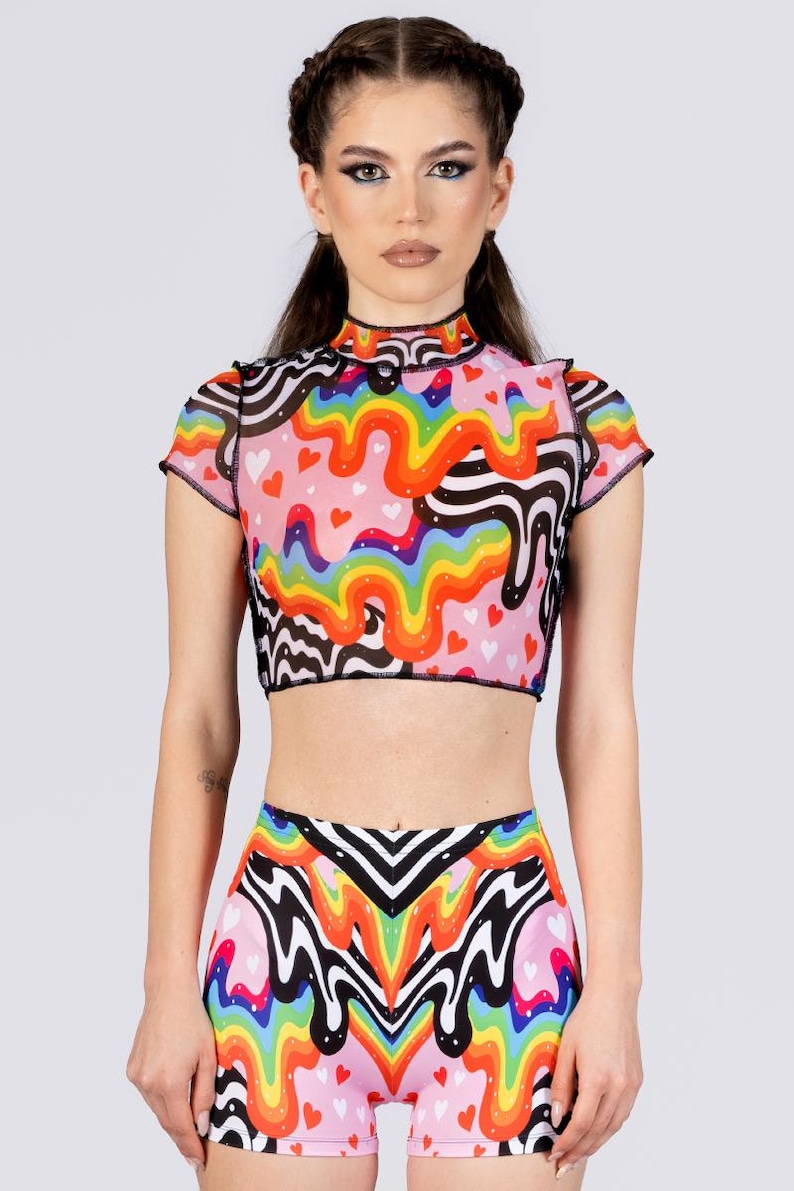 May include: A two-piece outfit featuring a crop top and shorts. The top has short sleeves and a high neck, with a pink base and a colorful rainbow and black wavy pattern. The shorts have a matching design with a rainbow and heart pattern.