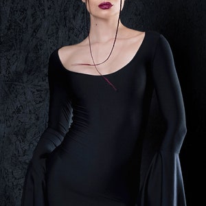 May include: A woman wearing a black long-sleeved dress with bell sleeves. She has dark hair and is wearing red lipstick.