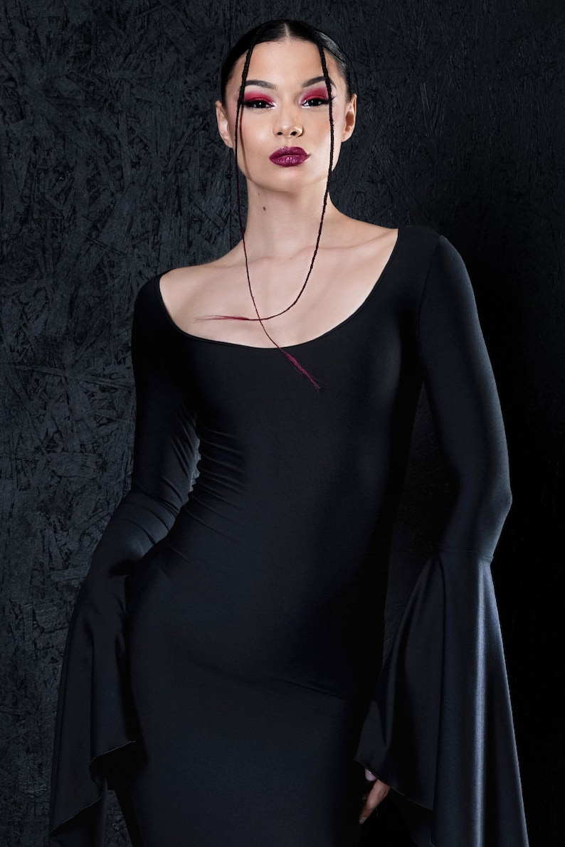 May include: A woman wearing a black long-sleeved dress with bell sleeves. She has dark hair and is wearing red lipstick.