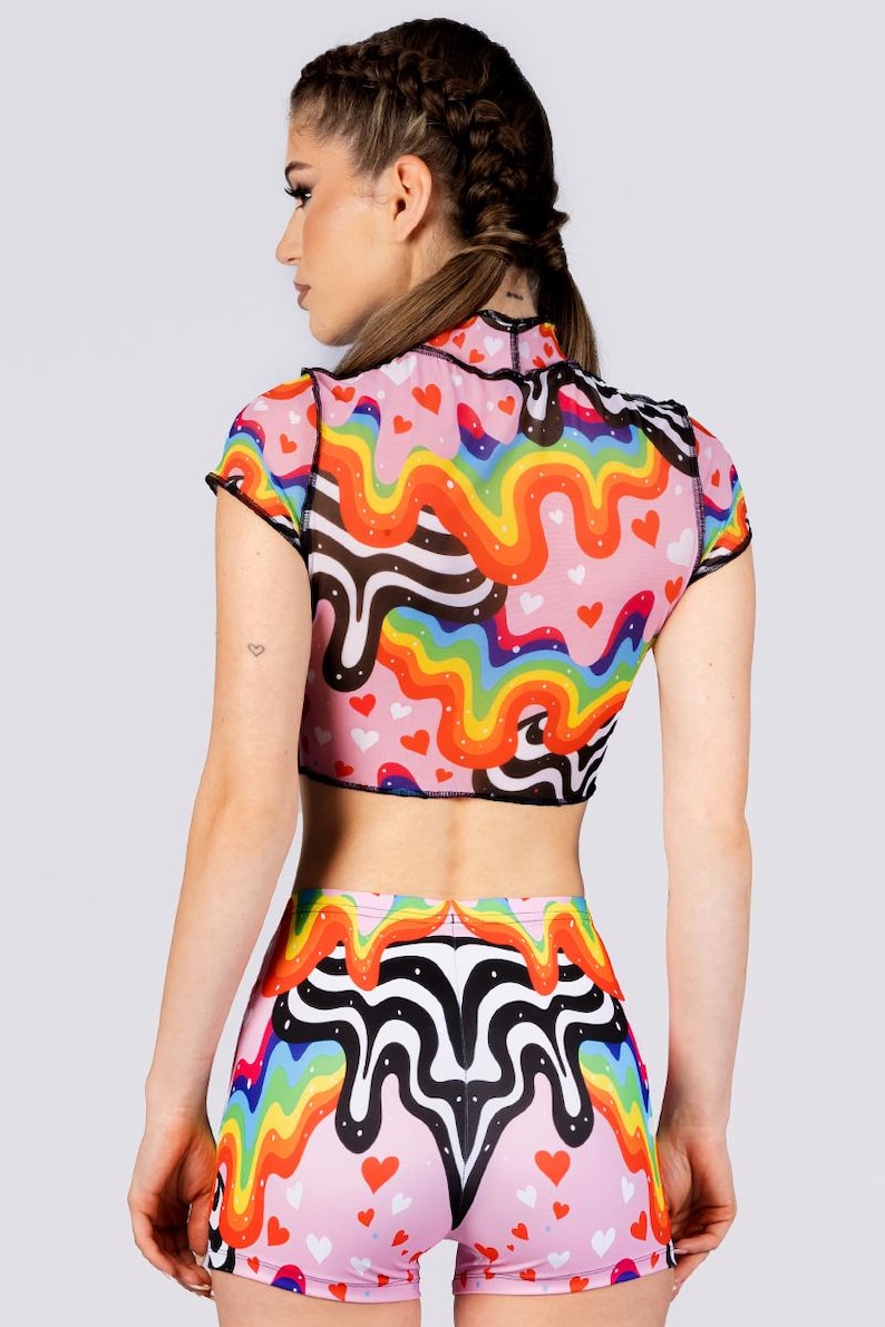 May include: A pink crop top and matching shorts set with a colorful rainbow and heart pattern. The top has short sleeves and a high neck, with black trim. The shorts are high-waisted and feature the same design.