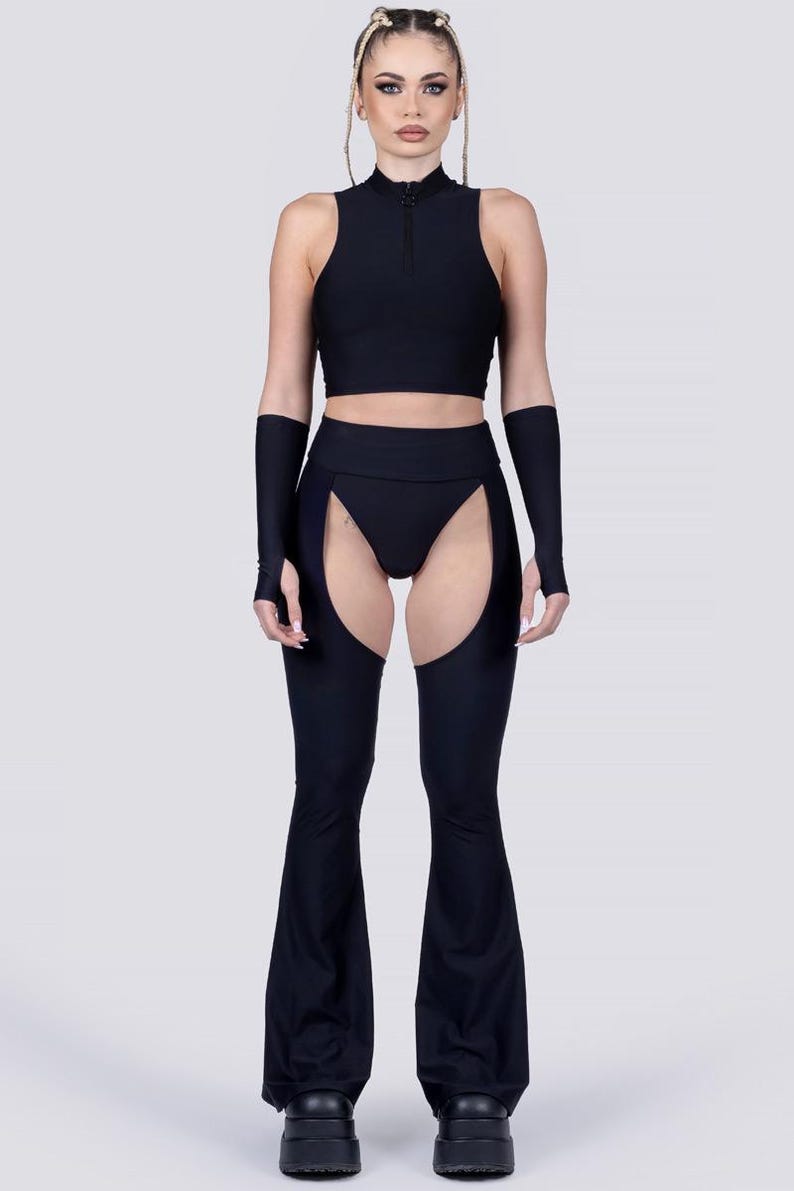 May include: Black two-piece outfit. The top is a sleeveless crop top with a high neck and a zipper. The bottoms are high-waisted with cutouts on the sides and flared legs. The outfit includes matching arm sleeves.