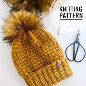 May include: A mustard yellow knitted beanie with a large brown and black faux fur pom pom. The beanie has a ribbed knit pattern and a brown leather tag that says "Weird Sheep".