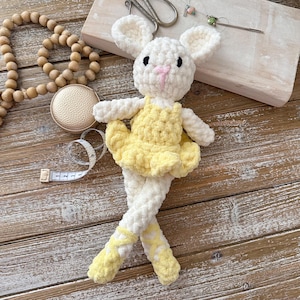 May include: A handmade white crochet bunny doll wearing a yellow tutu and ballet slippers. The bunny has black eyes and a pink nose. The doll is posed with its legs crossed, giving it a ballerina appearance.