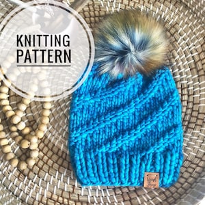 May include: Knitting pattern for a blue beanie with a fluffy brown and white pom pom. The beanie has a woven texture and a brown leather tag with the text "Weird Sheep".