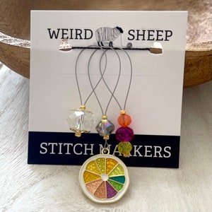 May include: Set of four stitch markers with colourful glass beads and a gold metal lemon slice charm. The card reads "Weird Sheep Stitch Markers".