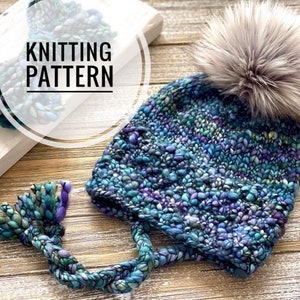 May include: A hand-knitted hat with a faux fur pom-pom. The hat is a mix of blue, green, and purple yarns. The image also includes the text "KNITTING PATTERN" in a white circle.