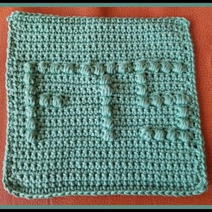 May include: A green crocheted dishcloth with the word "MOM" in raised stitches.