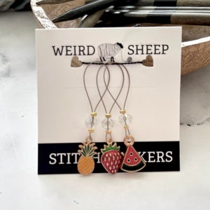 May include: Set of three stitch markers featuring a pineapple, strawberry and watermelon design. Each marker has a clear bead and a gold-coloured loop. The card reads "Weird Sheep Stitch Markers".