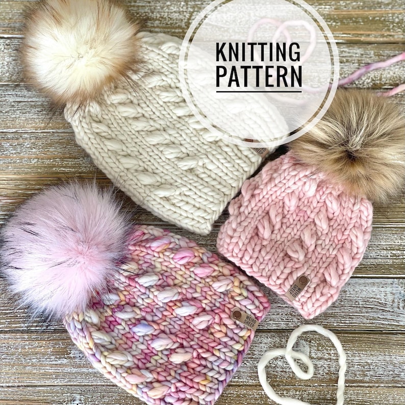 Puede incluir: Tres gorros de punto con pompones de piel sint&eacute;tica. Los gorros son en tonos de rosa y blanco. Los gorros est&aacute;n sobre una superficie de madera. El texto "Knitting Pattern" es visible en la imagen.
