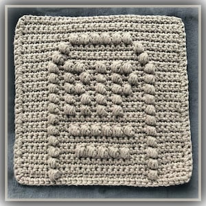 Peut inclure: Un coussin carré en crochet de couleur marron avec un motif texturé.