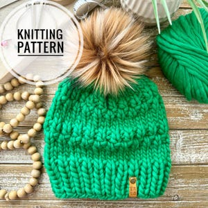 May include: A bright green chunky knit beanie featuring a large, fluffy faux fur pom-pom in shades of brown and tan. The hat has a thick, textured stitch pattern and a small rectangular leather tag labelled "WEIRD SHEEP" at the bottom edge.