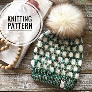 May include: A green and white knitted hat with a fluffy white pom pom. The hat has a checkered pattern and a label that says "Weird Sheep".