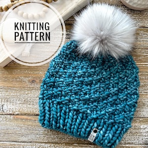 May include: Teal blue knitted beanie with a white faux fur pom pom. The beanie has a woven label that says "WEIRD STREETS".