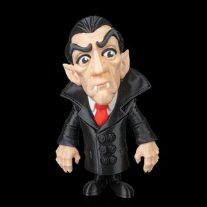 Puede incluir: Figura del Conde Drácula, con un abrigo negro con botones grandes y una corbata roja. La figura tiene piel pálida, cabello oscuro y colmillos. El fondo es negro. Objeto de colección.