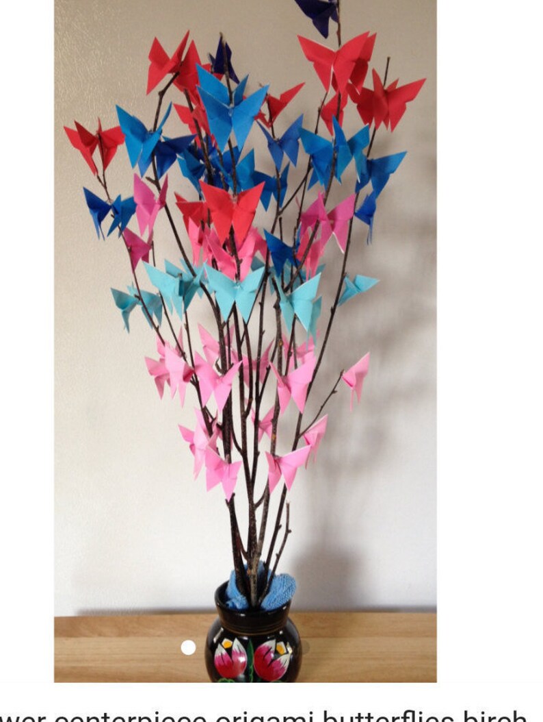 May include: A decorative arrangement of branches adorned with origami butterflies in shades of red, blue, and pink. The branches are placed in a dark vase with floral designs, creating a colorful and artistic centerpiece.